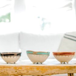 Three clay bowls with colourful woven edges on wood table
